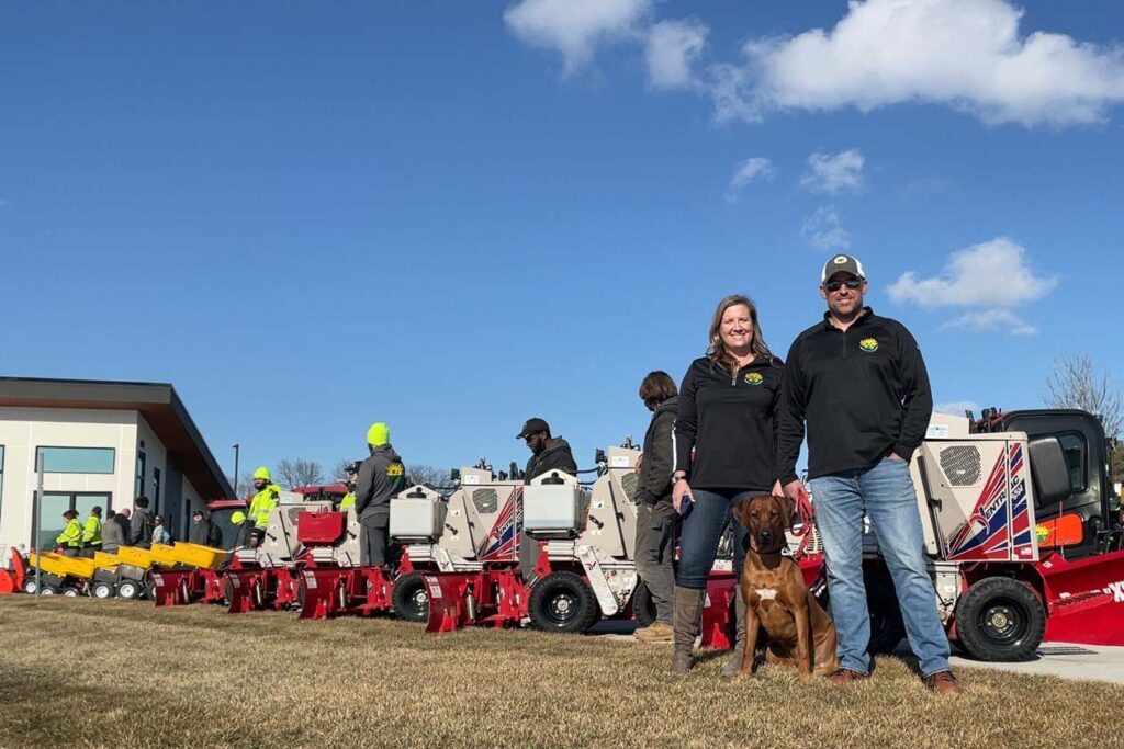 the owners of RJ Lawn and their dog standing in front of snow removal vehicles