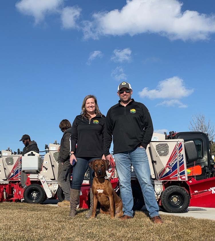the owners of RJ Lawn and their dog standing in front of snow removal vehicles